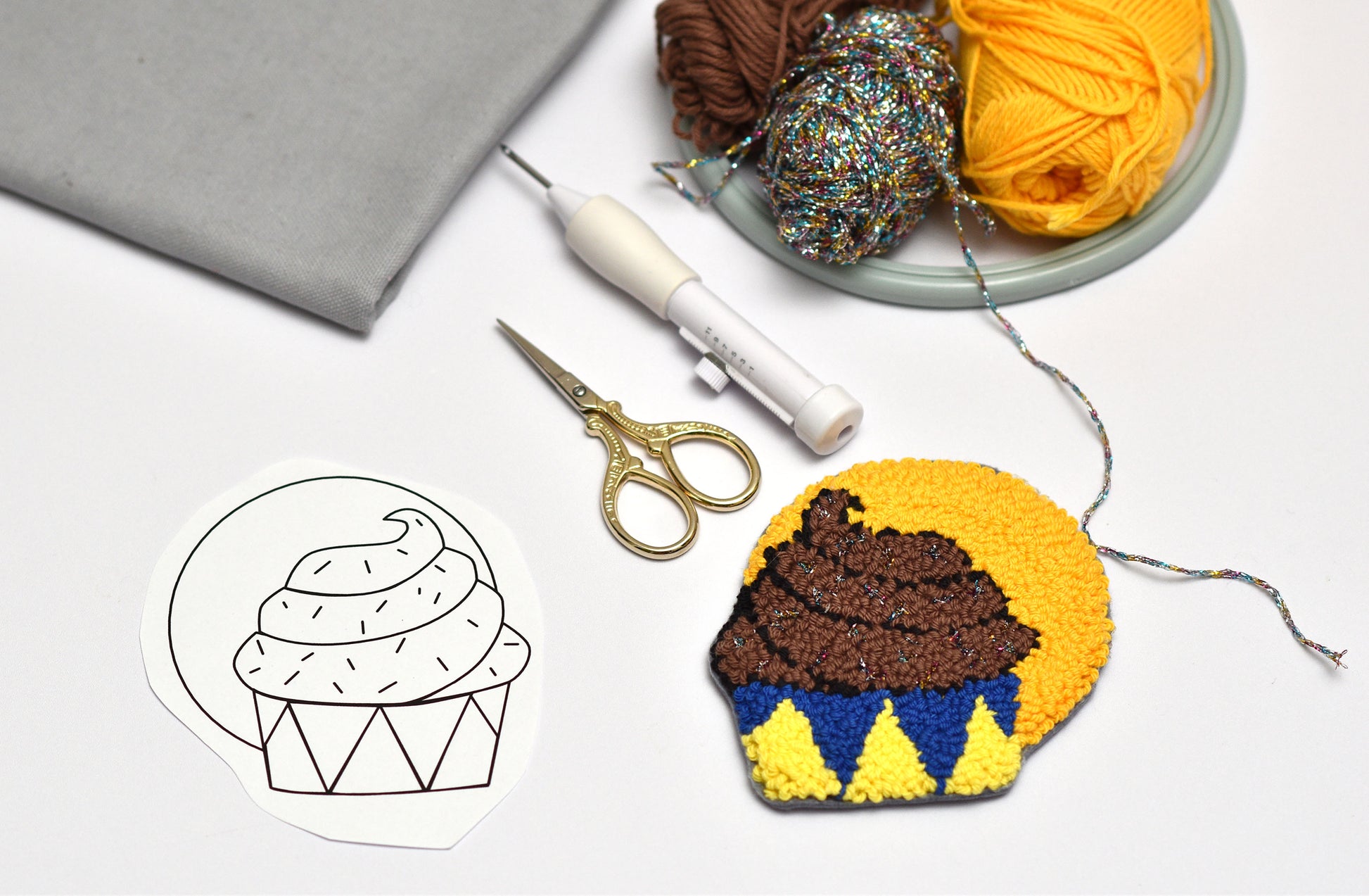 Embroidered cupcake coaster with yarn, scissors, and a pattern on a white background