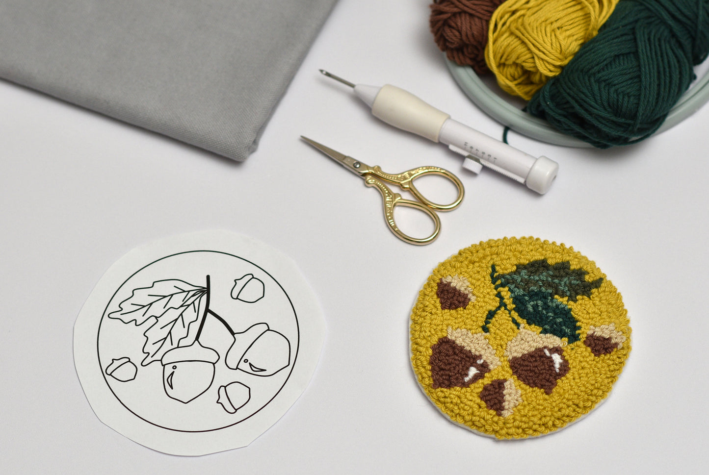 Embroidery hoop with a completed design of hazelnuts and leaves, scissors, and yarn on a gray surface.