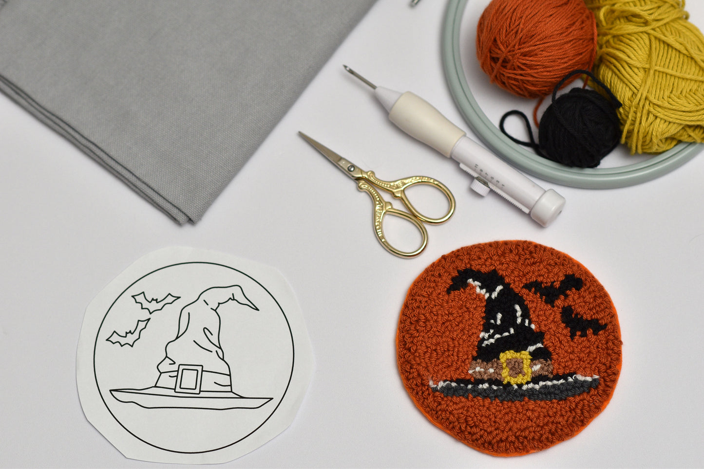 Witch hat design coaster on a round brown fabric patch with yarn, scissors, and a template on a gray surface.
