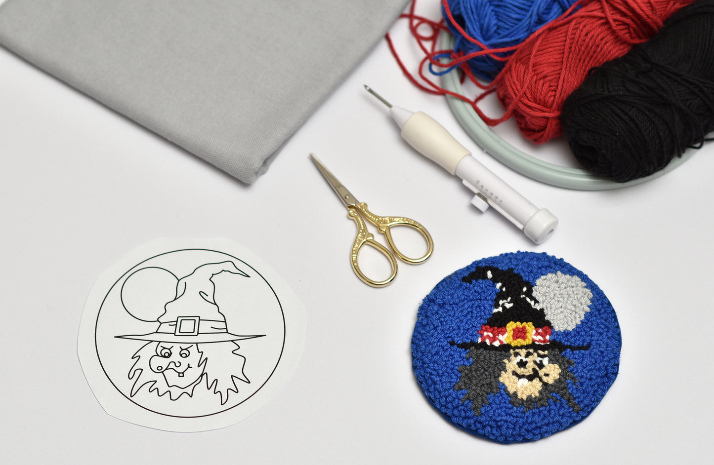 Embroidery hoop with Halloween-themed Witch design coaster, scissors, and yarn on a white surface