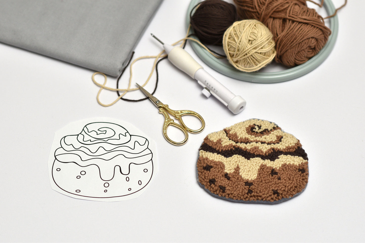 Embroidered cinnamon roll with yarn, scissors, and a pattern on a white background