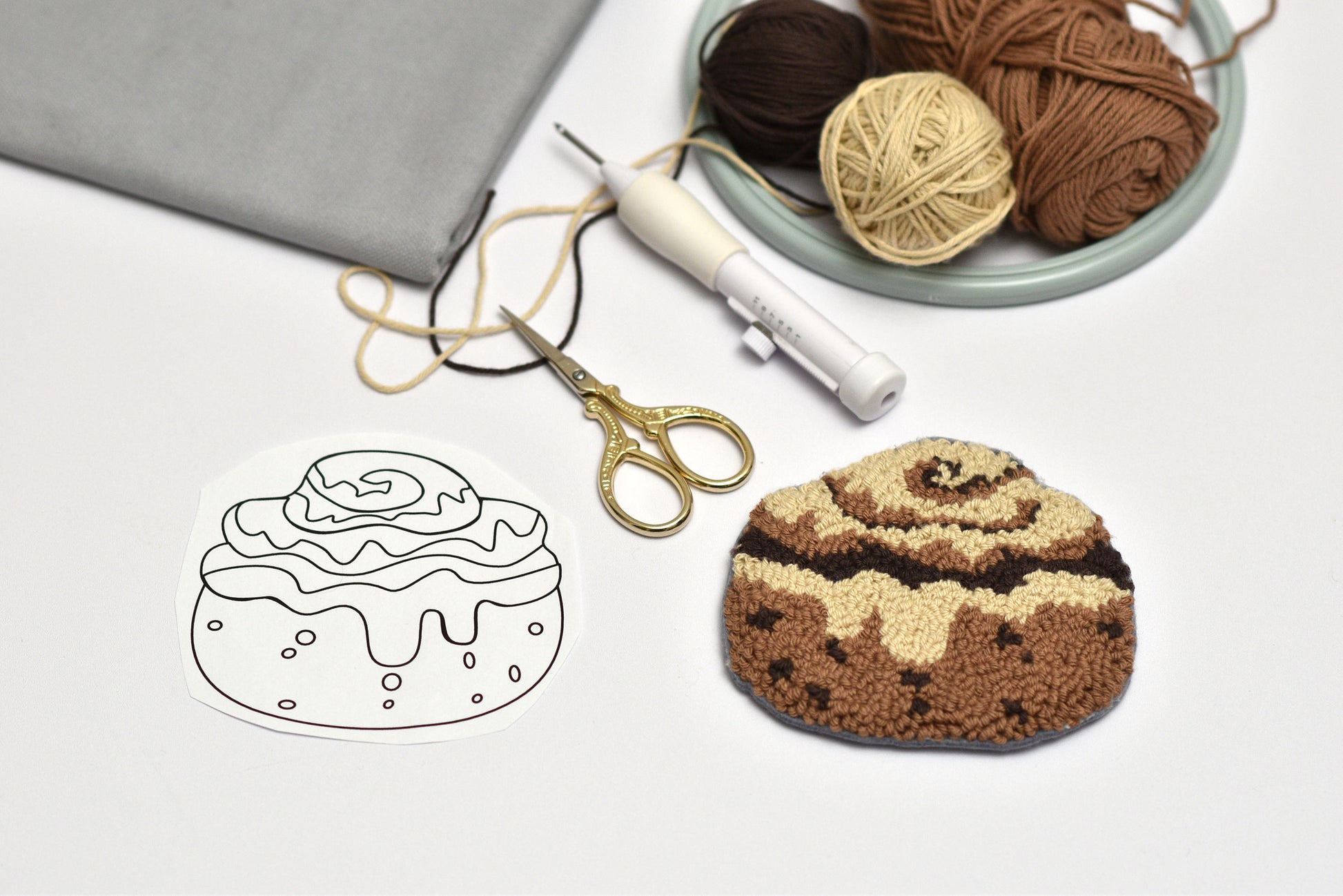 Embroidered cinnamon roll with yarn, scissors, and a pattern on a white background