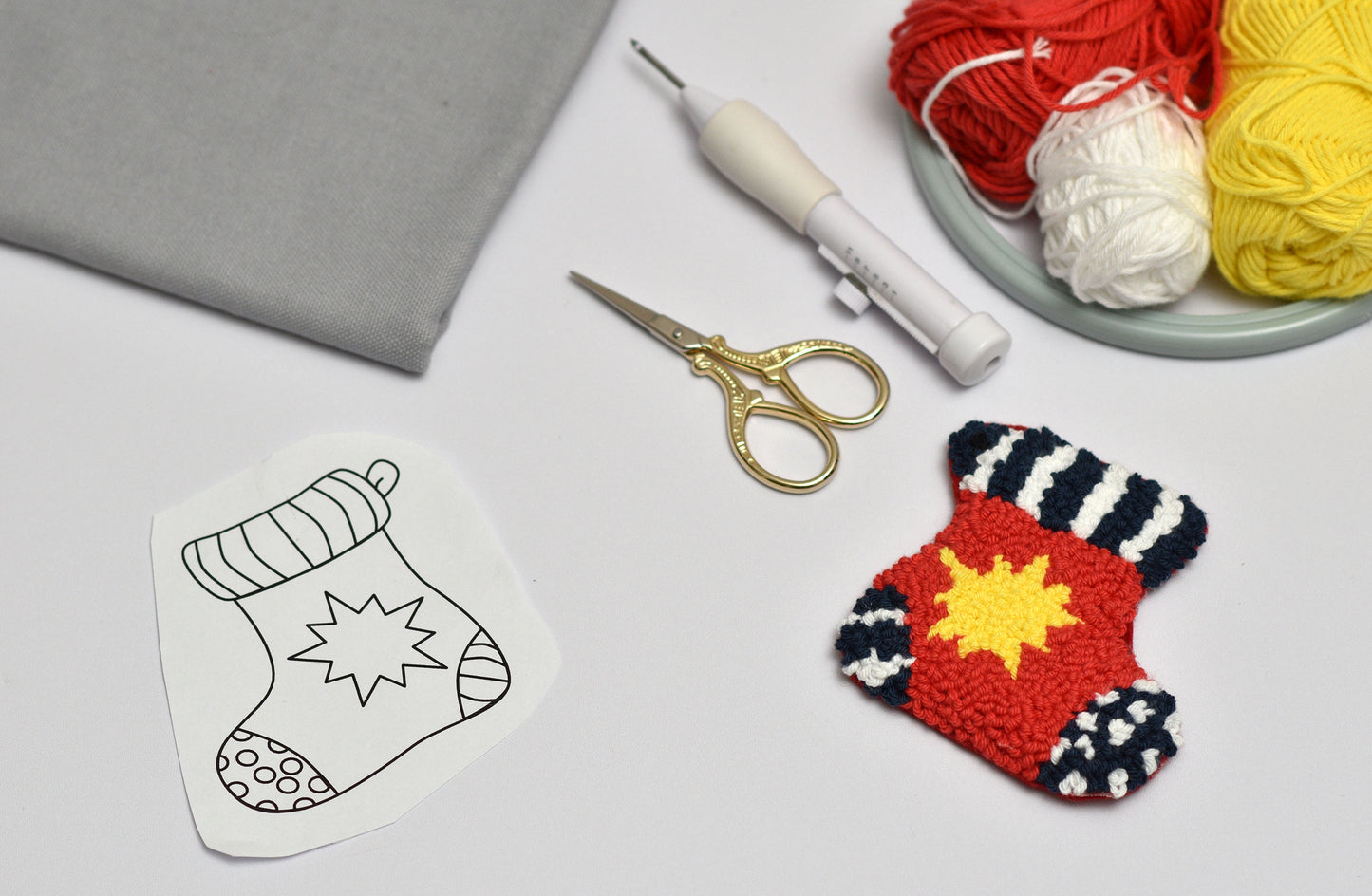 Embroidered stocking shaped coaster, scissors, and yarn on a light gray surface