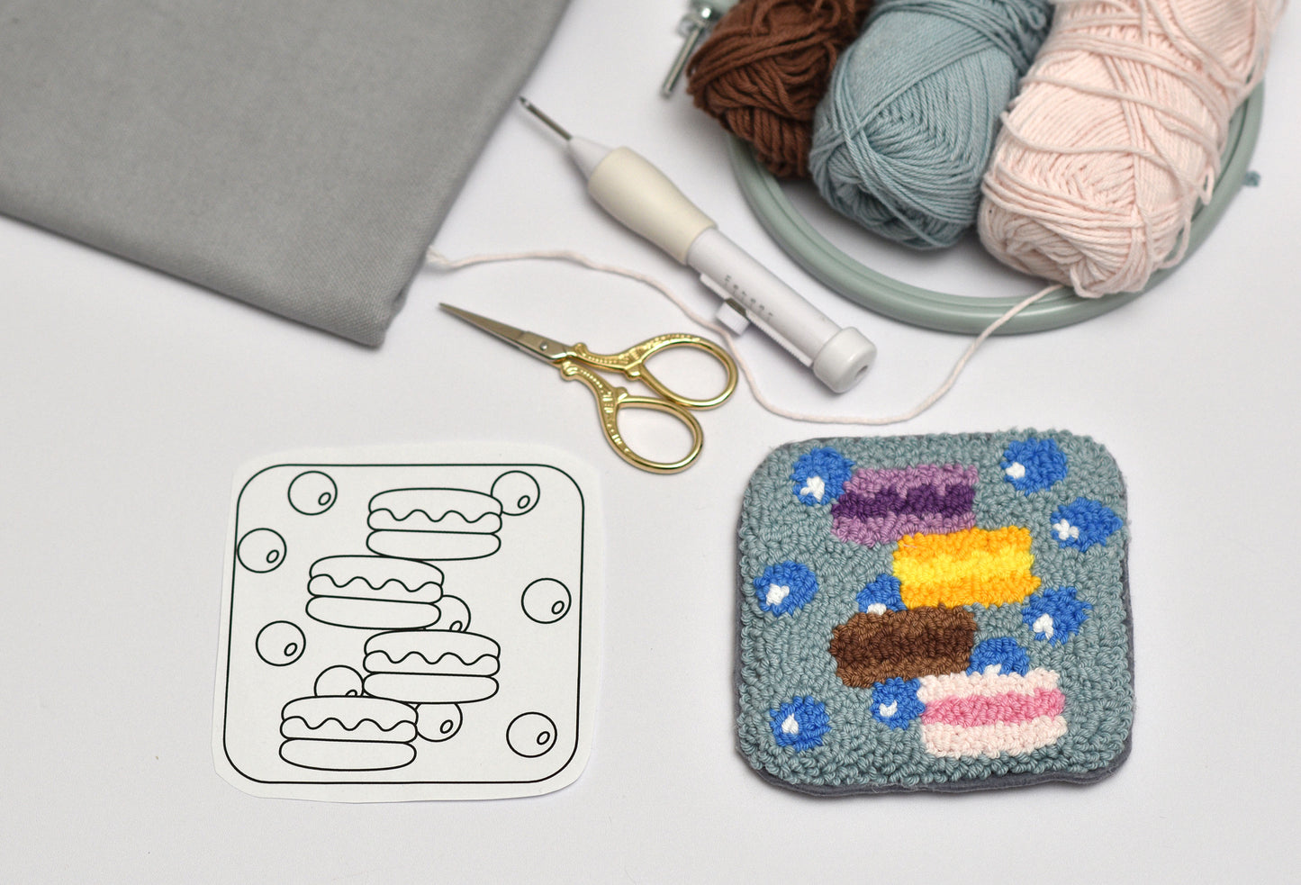 Embroidered coaster with colorful macaron design next to a coloring page and yarn on a light gray background