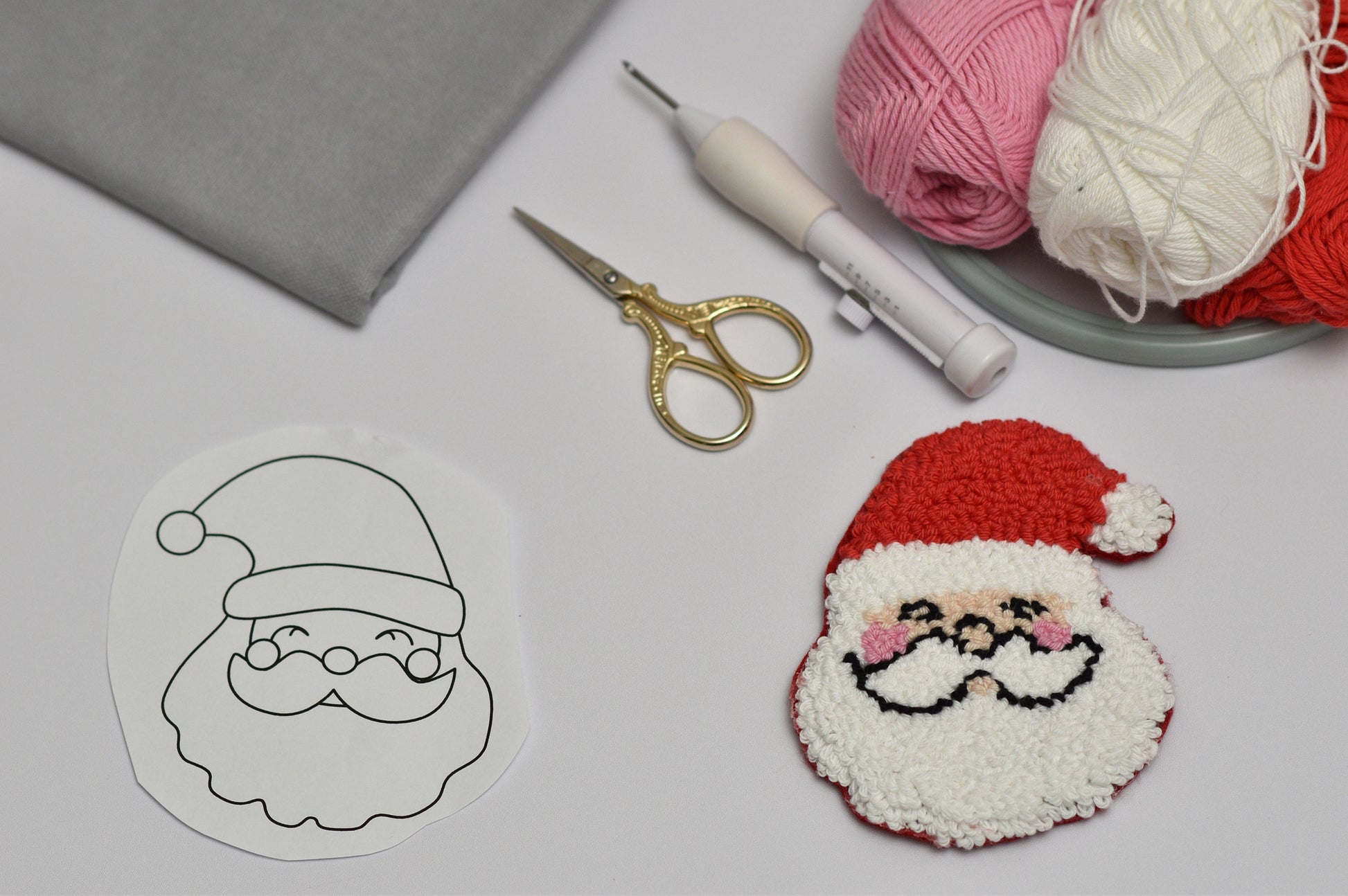 Santa Claus coaster design and punch needle project on a table with yarn and tools.