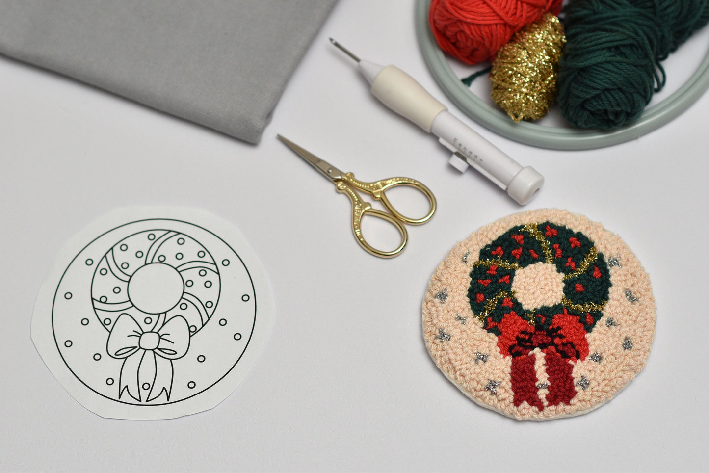 Embroidery hoop with a wreath design next to yarn and scissors on a gray surface