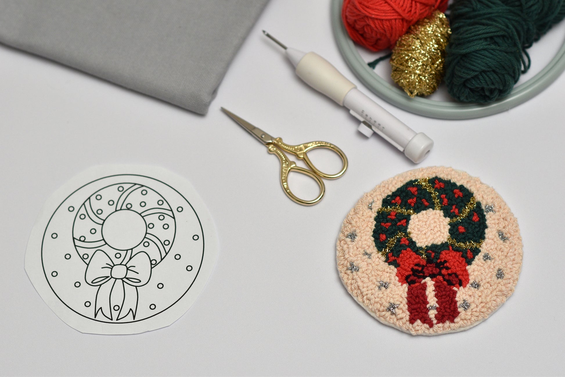 Embroidery hoop with a wreath design next to yarn and scissors on a gray surface