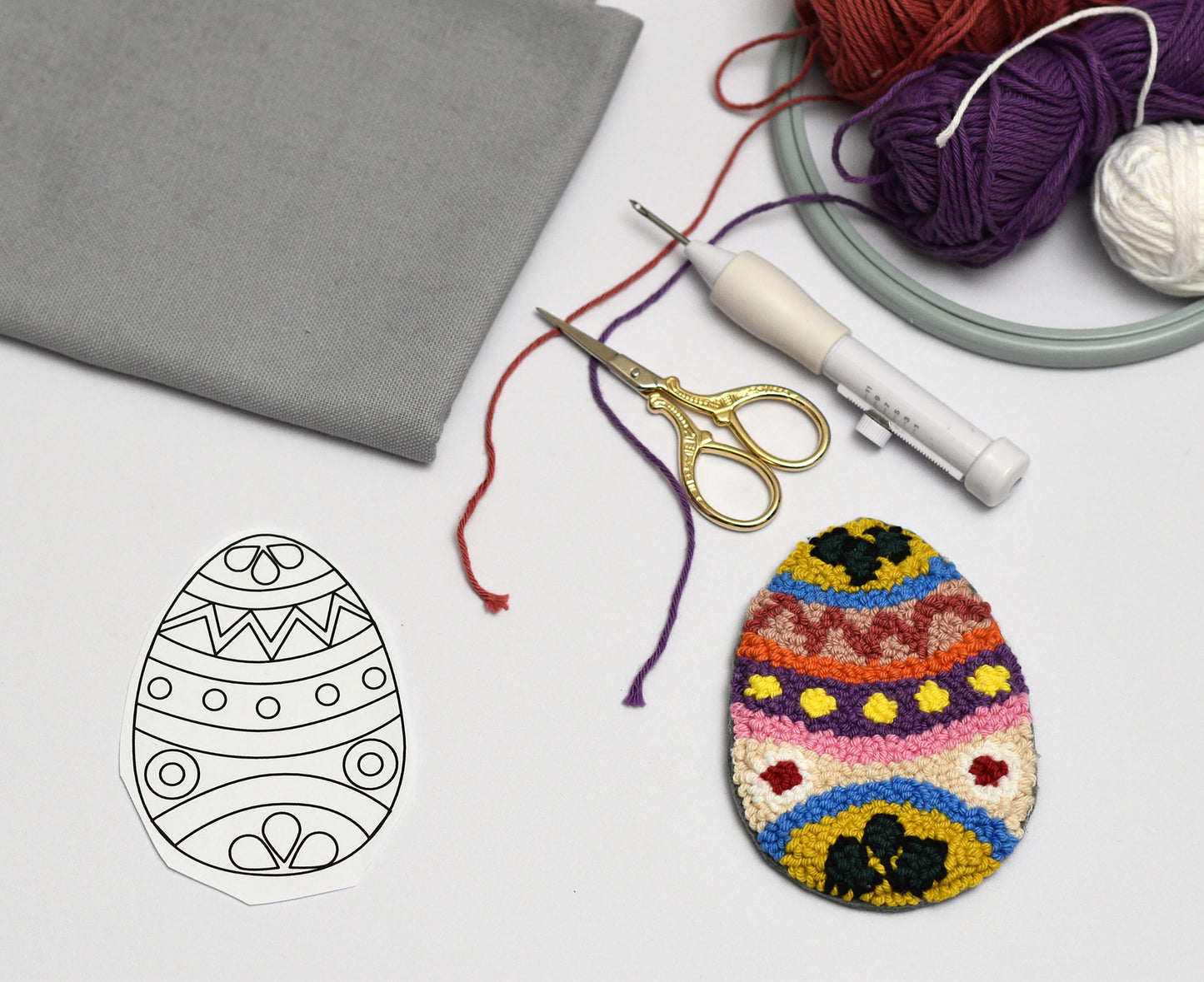 Colorful embroidered Easter egg with a template and crafting supplies on a white surface