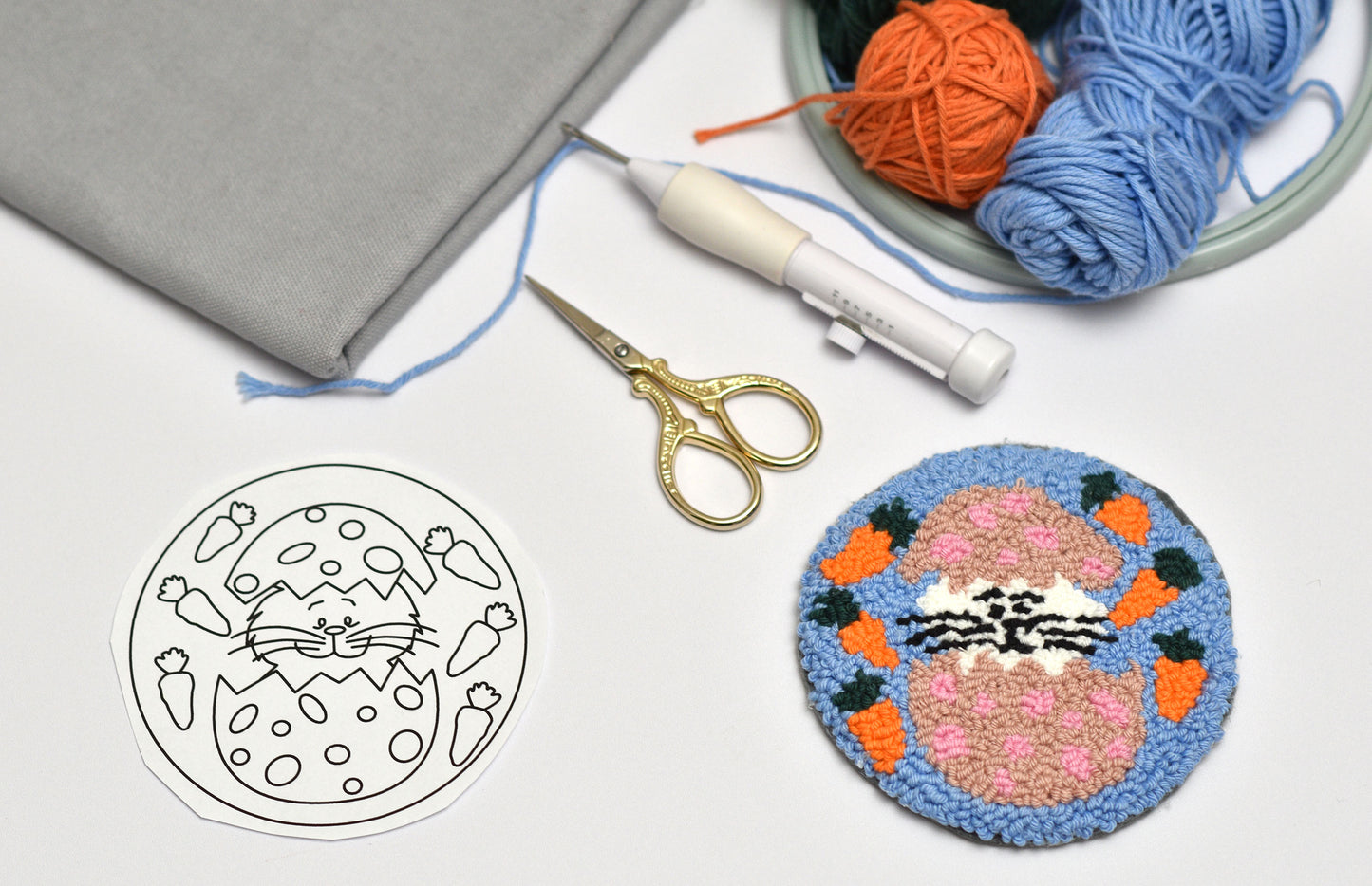 Embroidery hoop with embroidered design, yarn, scissors, and pattern on a white surface