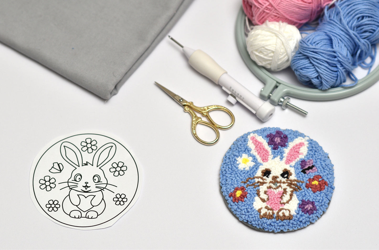 Embroidery hoop with a completed Easter bunny design, yarn balls, scissors, and a black and white outline of a bunny on a white background.
