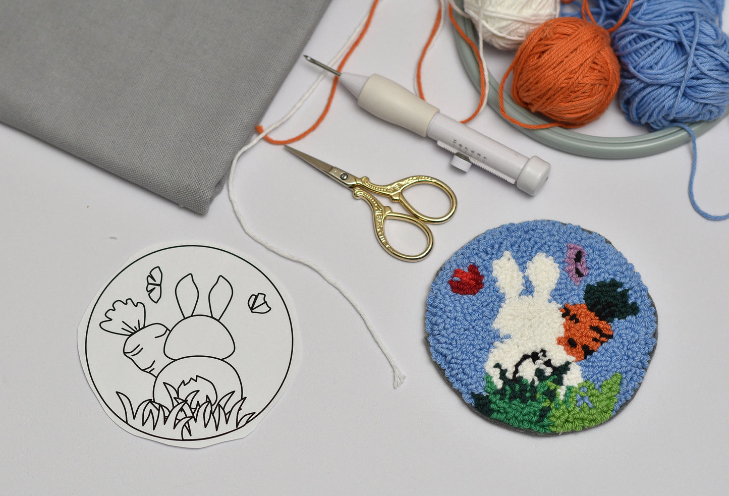 Embroidery hoop with a completed coaster of a bunny and flowers, next to a black and white outline drawing on fabric.