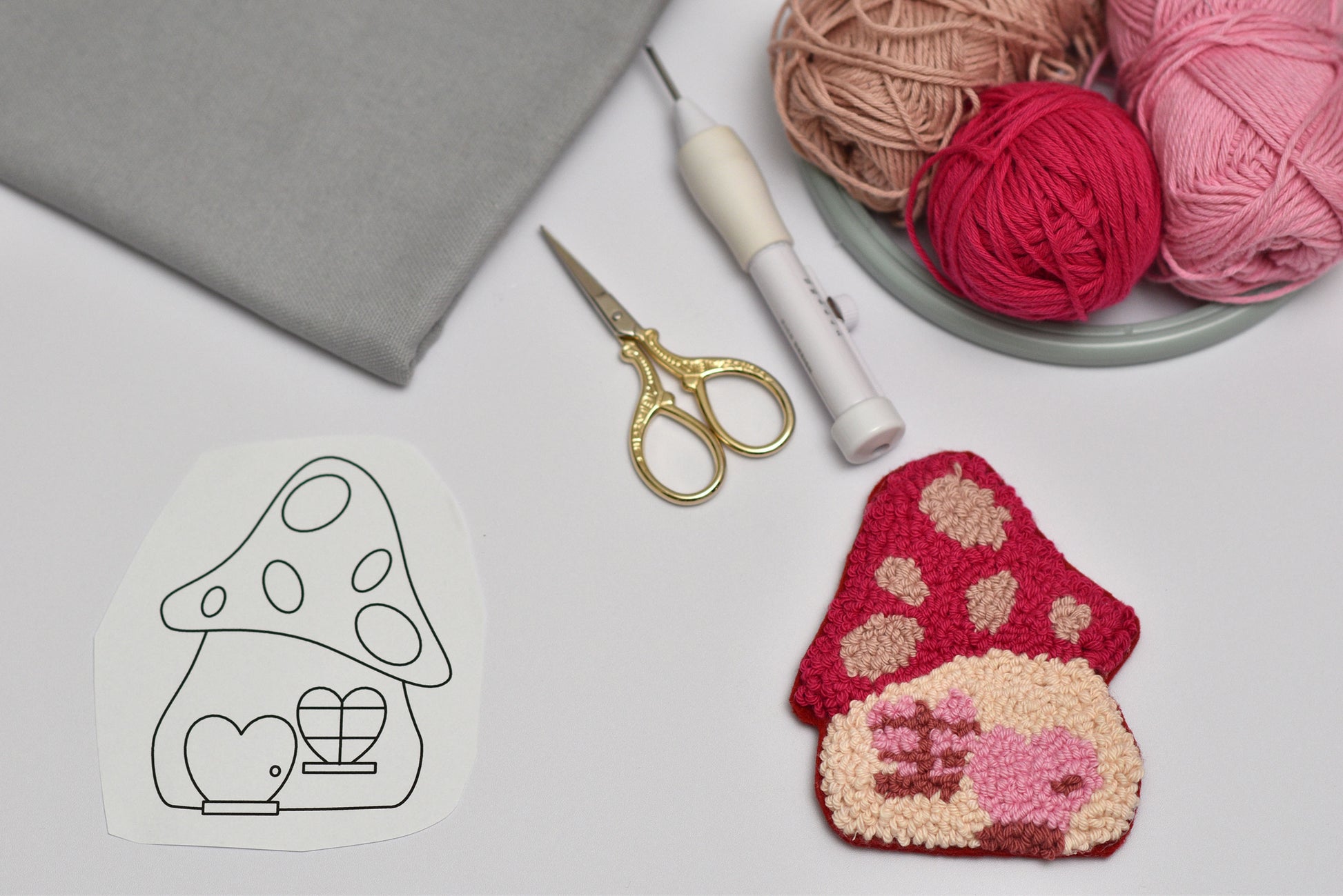 Embroidery hoop with mushroom design punch needle coaster, scissors, and yarn on a table