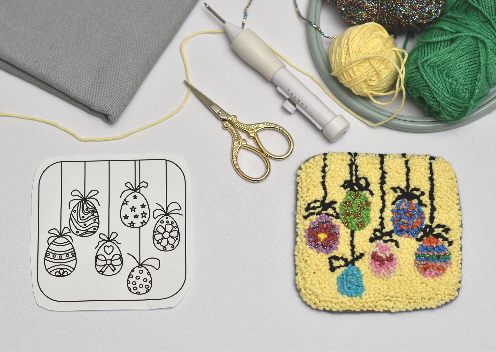 Embroidery Easter Eggs Coaster project with patterned card, yarn, scissors, and embroidery hoop on a gray surface.