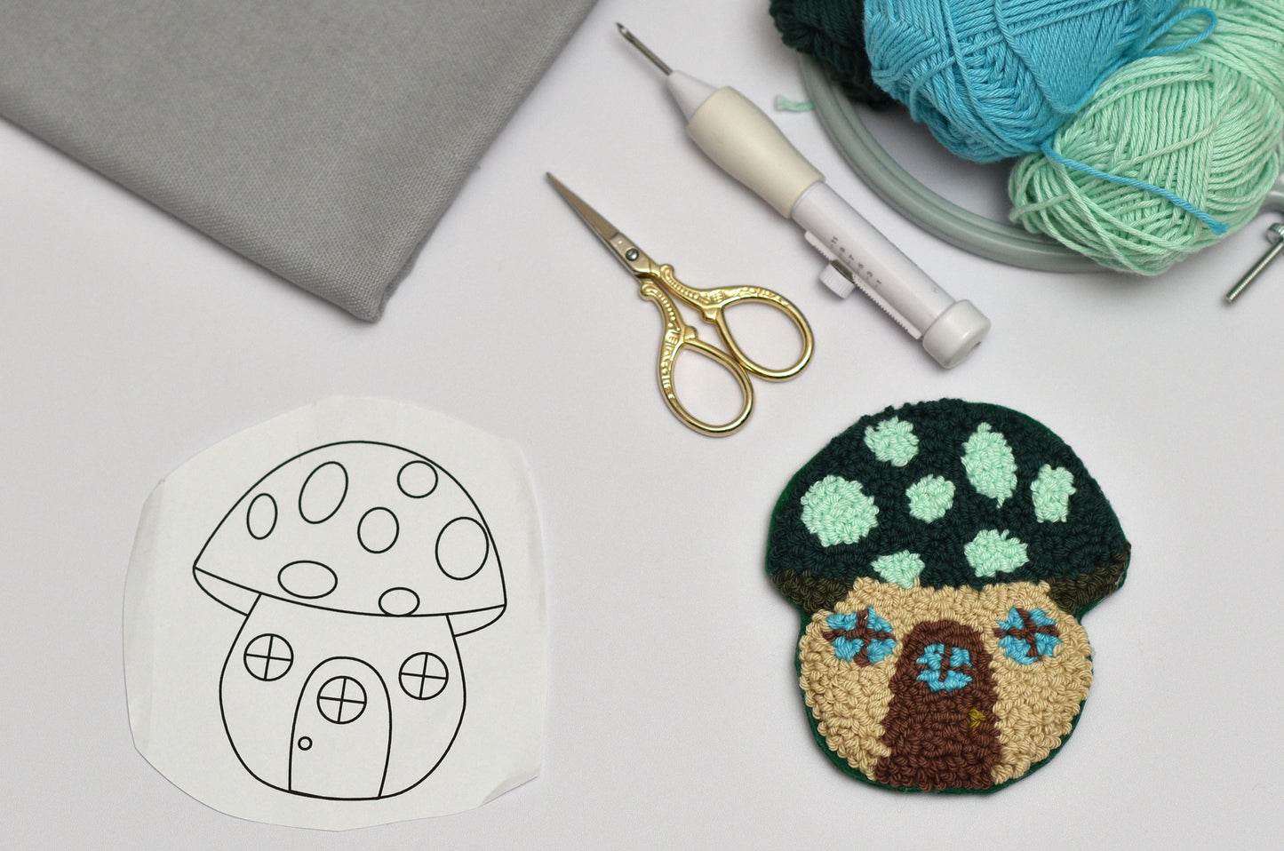 Embroidery hoop with mushroom design, completed mushroom punch needle coaster, scissors, and yarn on a white surface.
