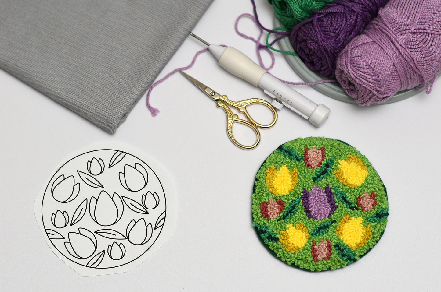 Embroidery hoop with floral tulip design, scissors, and yarn on a white surface