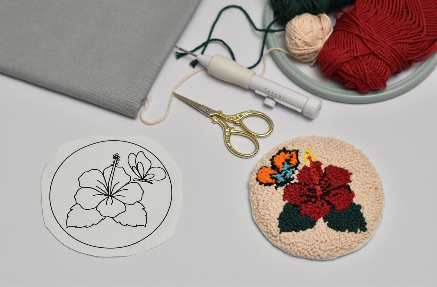 Embroidery hoop with floral hibiscus design, scissors, and yarn on a light surface
