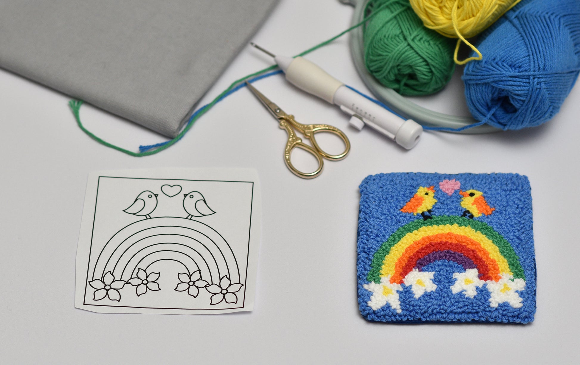 Embroidered coaster with birds design next to a coloring page and yarn on a white surface.