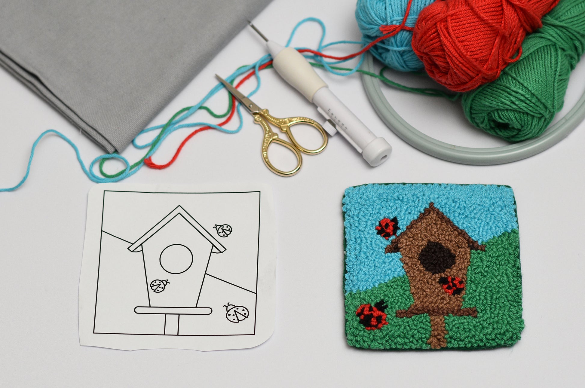 Embroidery coaster project with a birdhouse design on fabric and yarn nearby