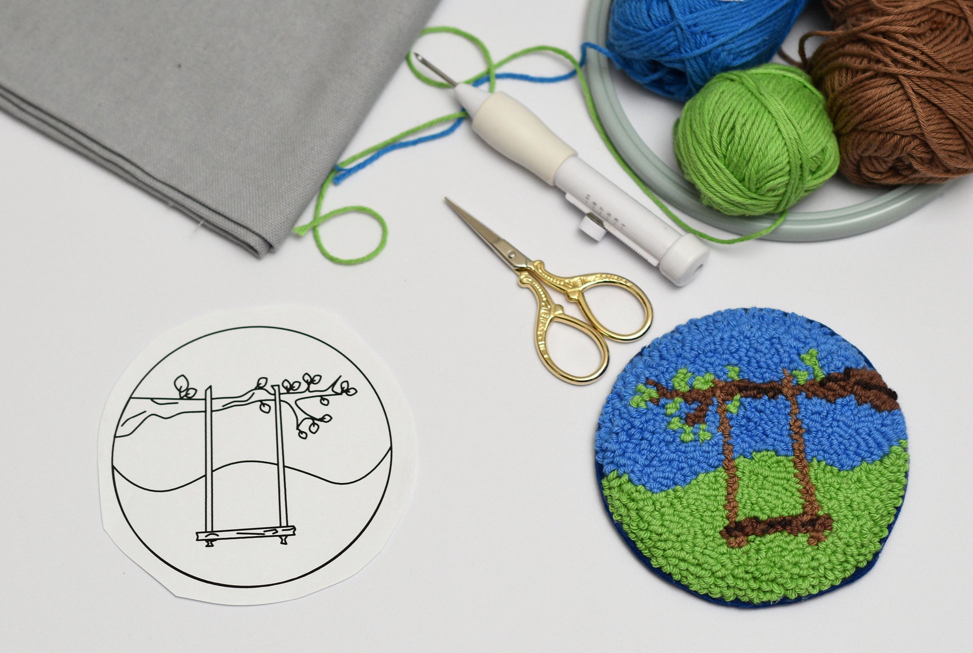 Crafting materials including yarn, scissors, and a completed mug rug punch needle project on a white surface.