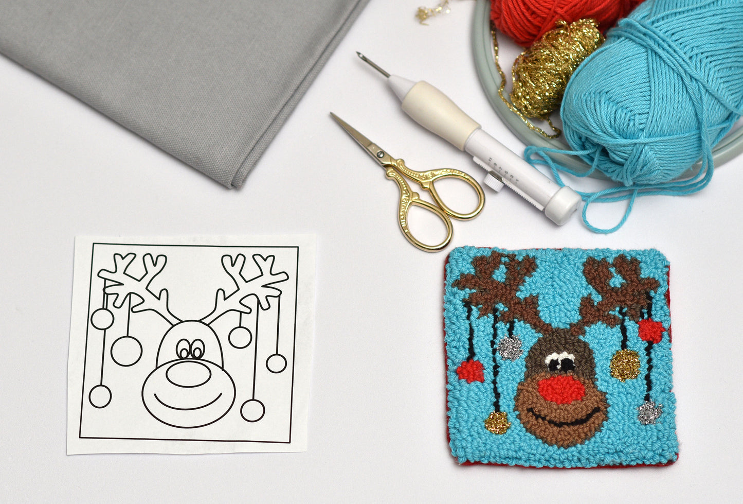 Punch needled reindeer coaster with yarn, scissors, and pattern on a white background