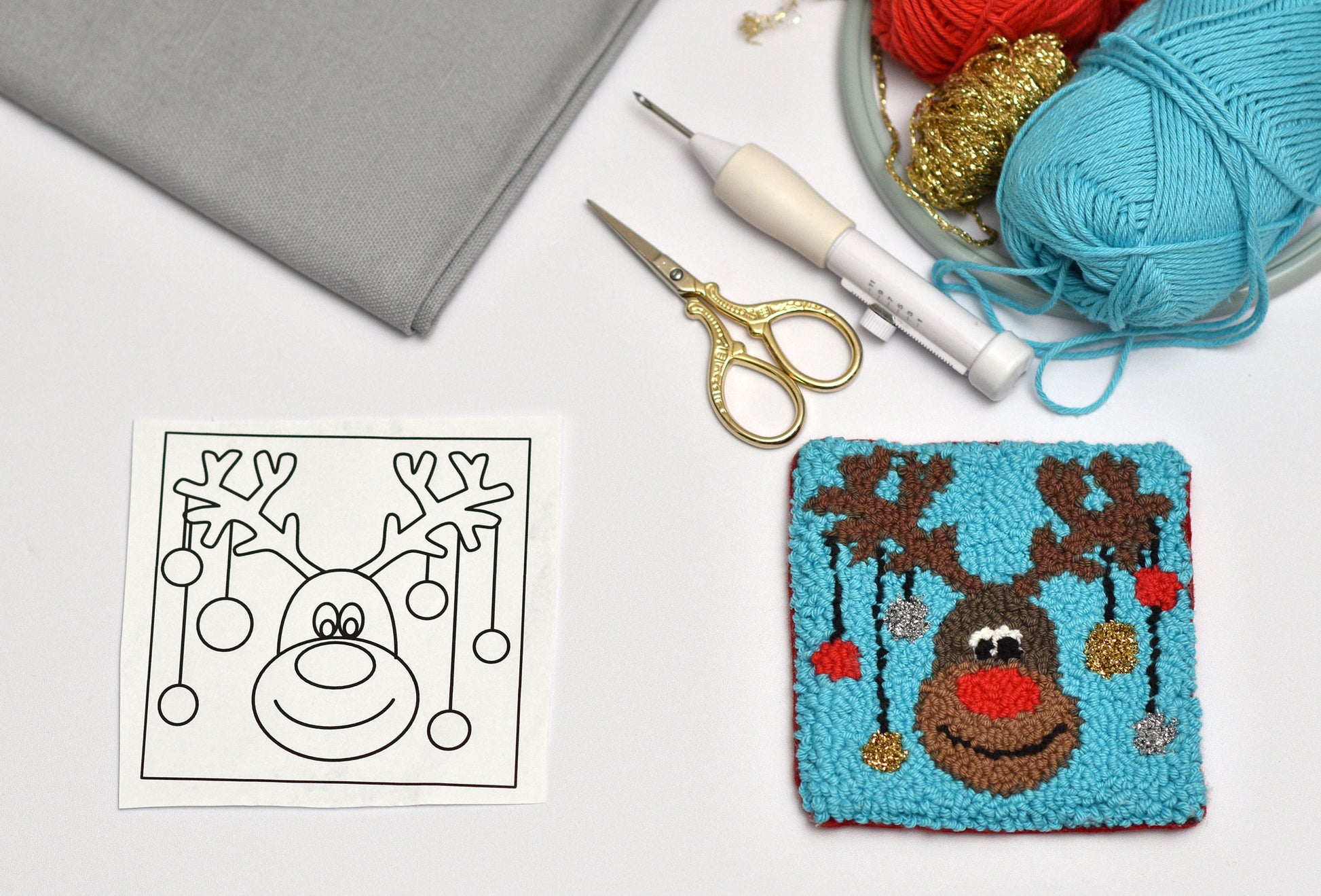 Punch needled reindeer coaster with yarn, scissors, and pattern on a white background
