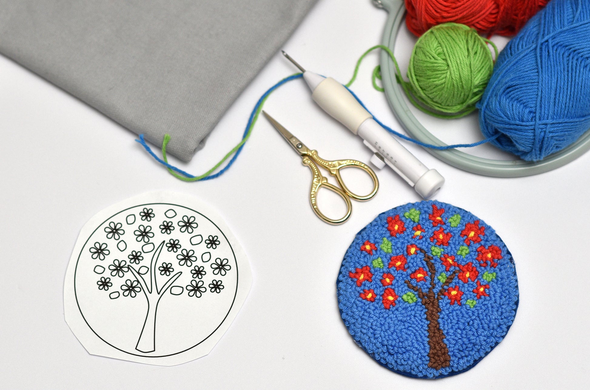 Embroidery hoop and a coaster with colorful tree design, scissors, and yarn on a white background