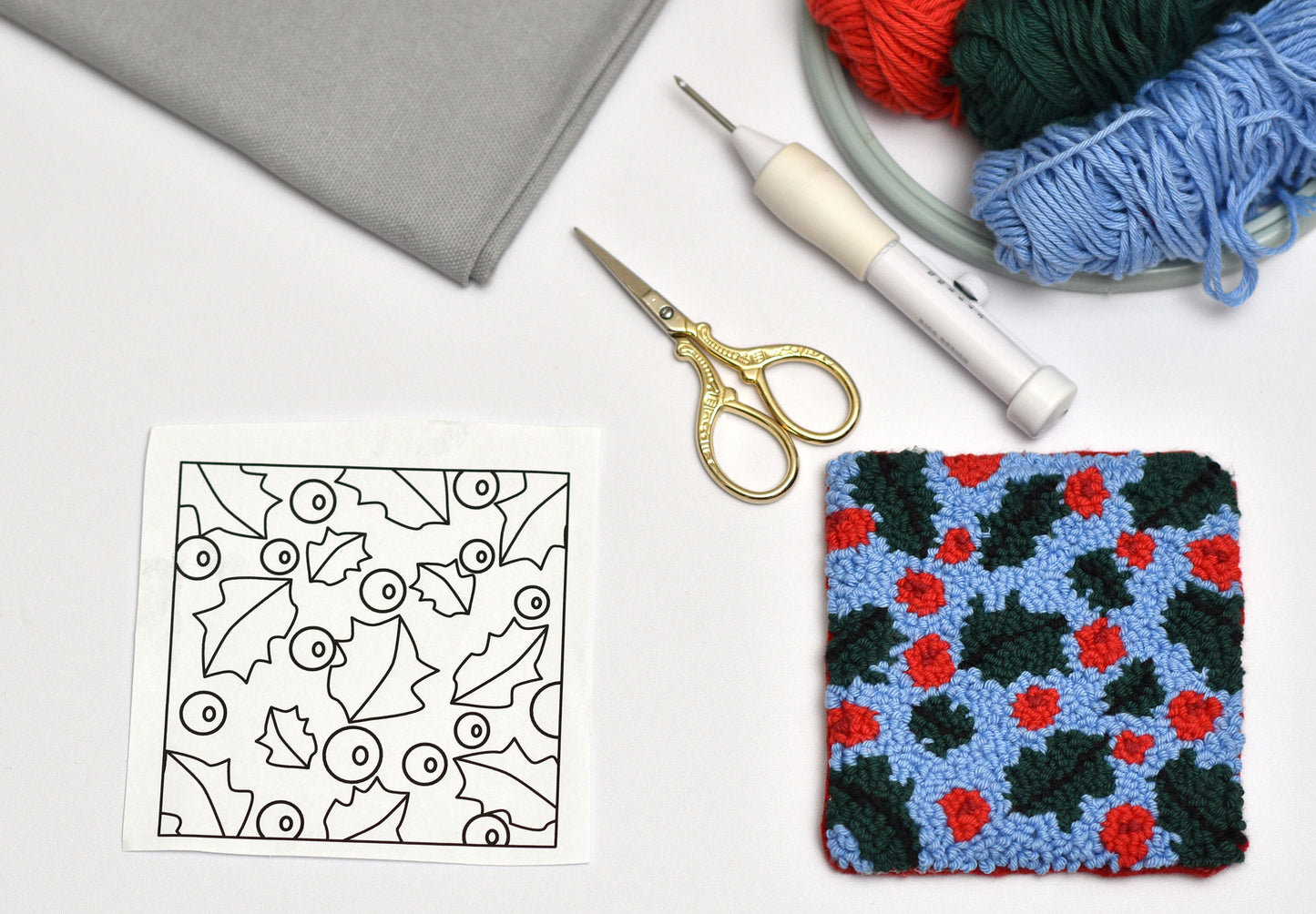 Punch needled square coaster with mistle toe floral pattern, coloring page, scissors, and yarn on a white surface