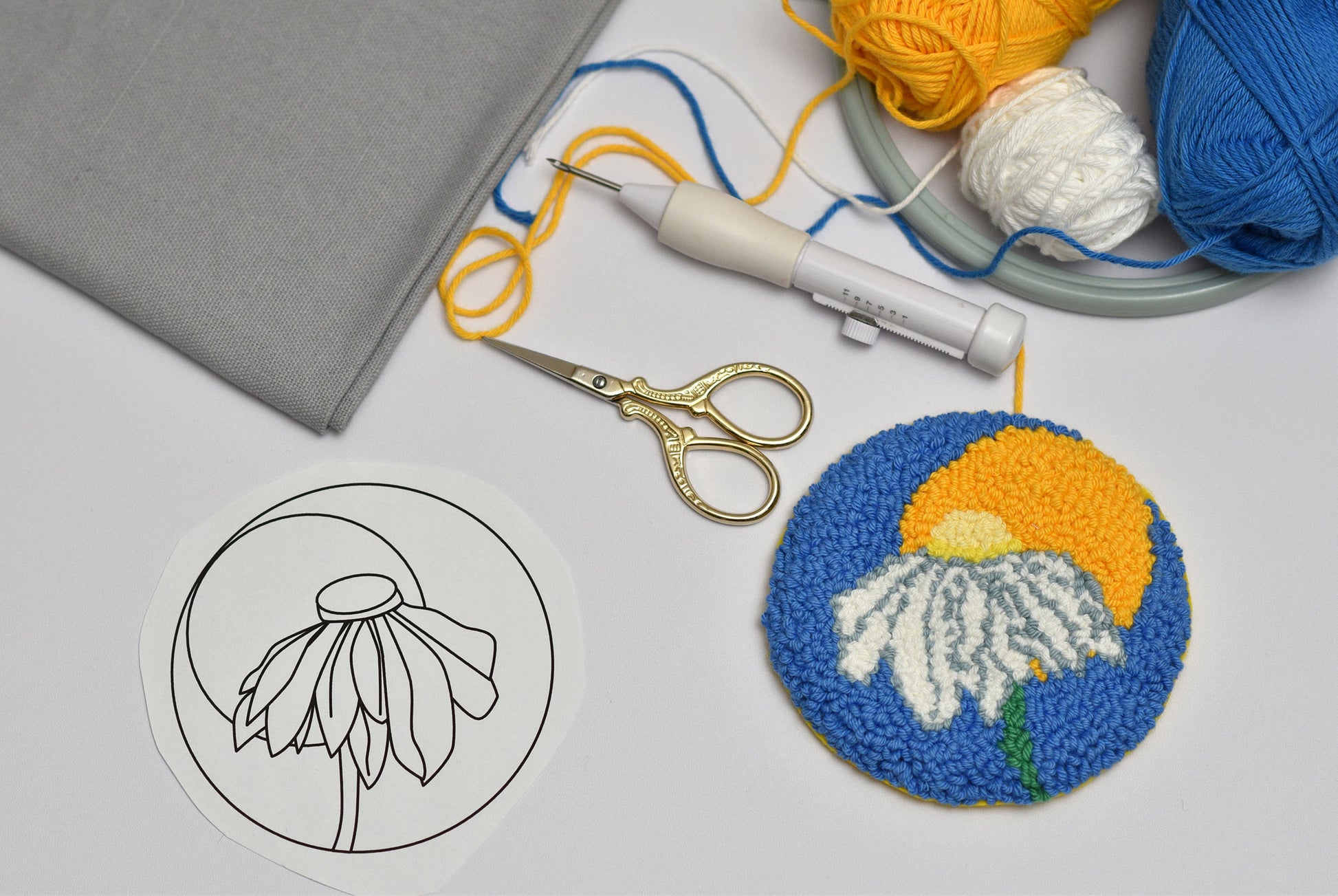 Embroidery hoop with coaster floral design, scissors, and yarn on a gray surface