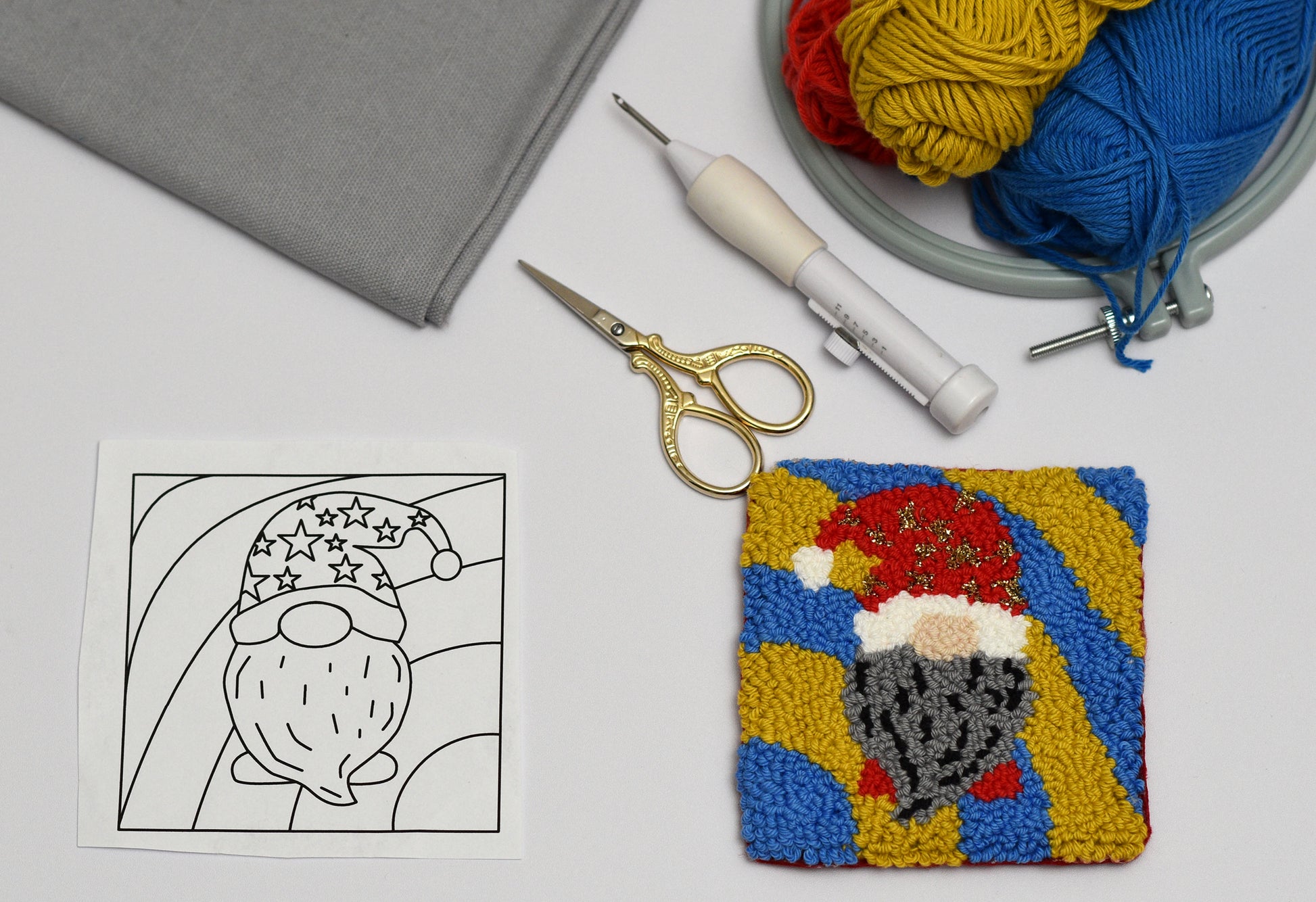 Colorful punch needle coaster of a gnome with a template and crafting tools on a white surface