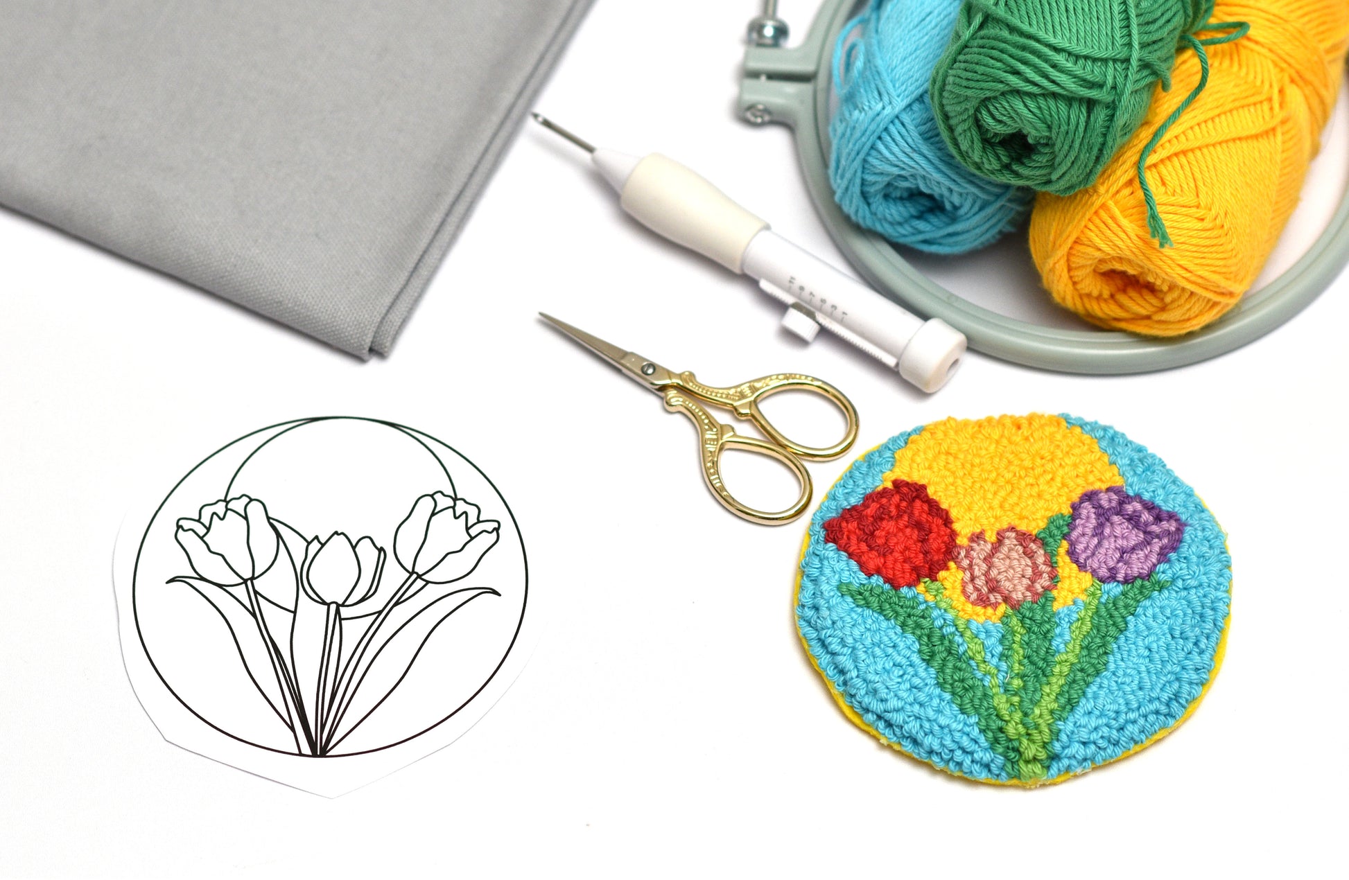 Embroidery hoop with colorful yarn, scissors, and embroidered flower design on a white background.