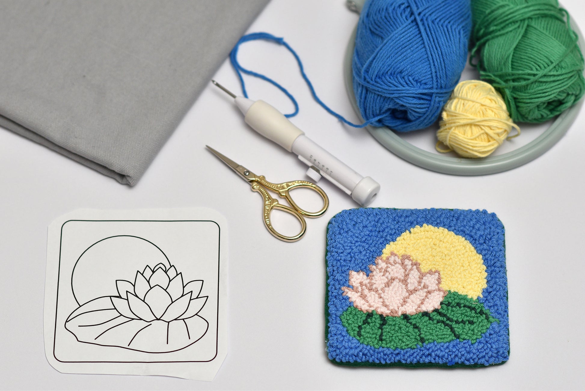 Punch needled lily flower coaster with yarn, scissors, and a template on a white surface