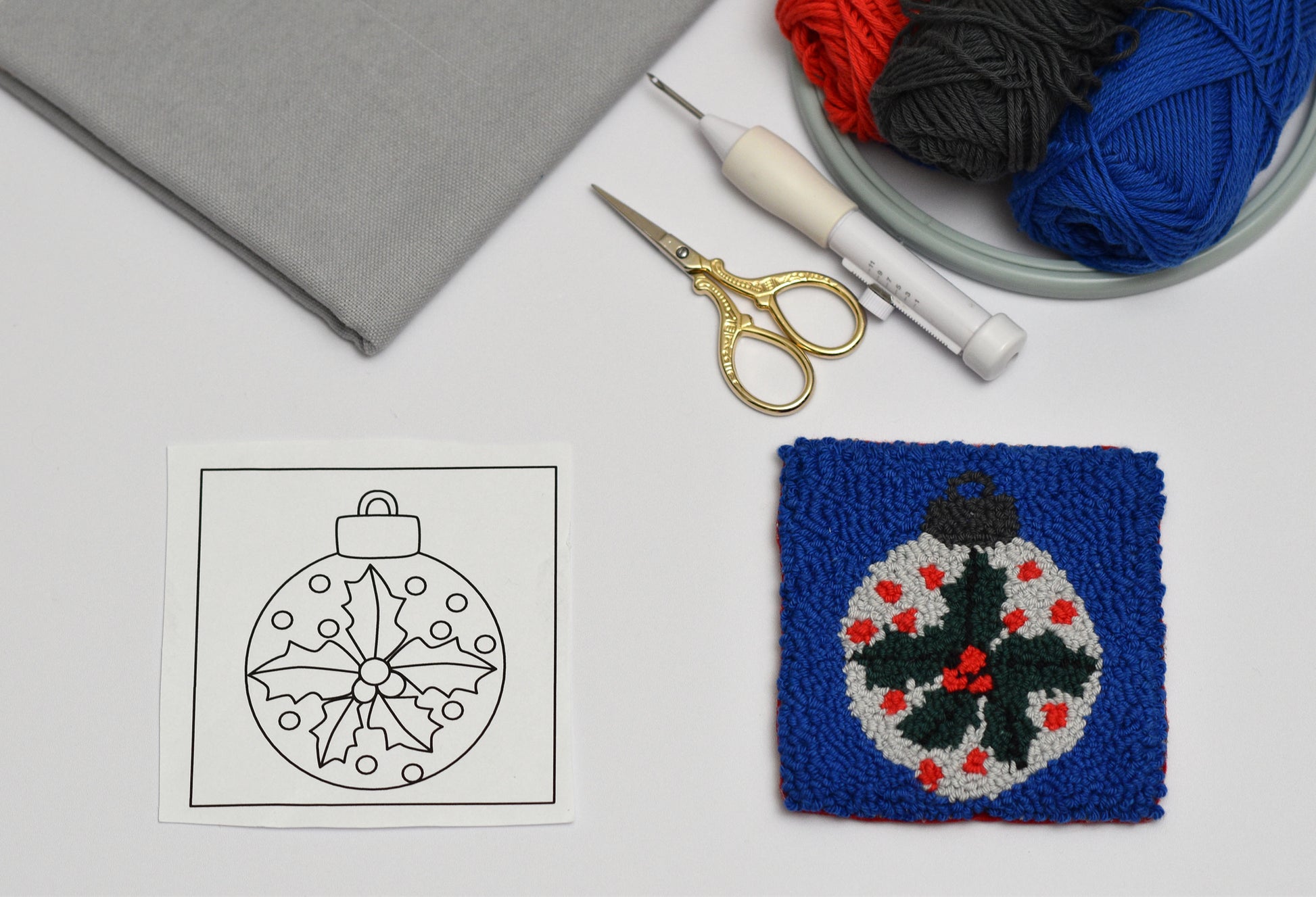 Punch needled coaster sample with yarn, scissors, and pattern on a white surface
