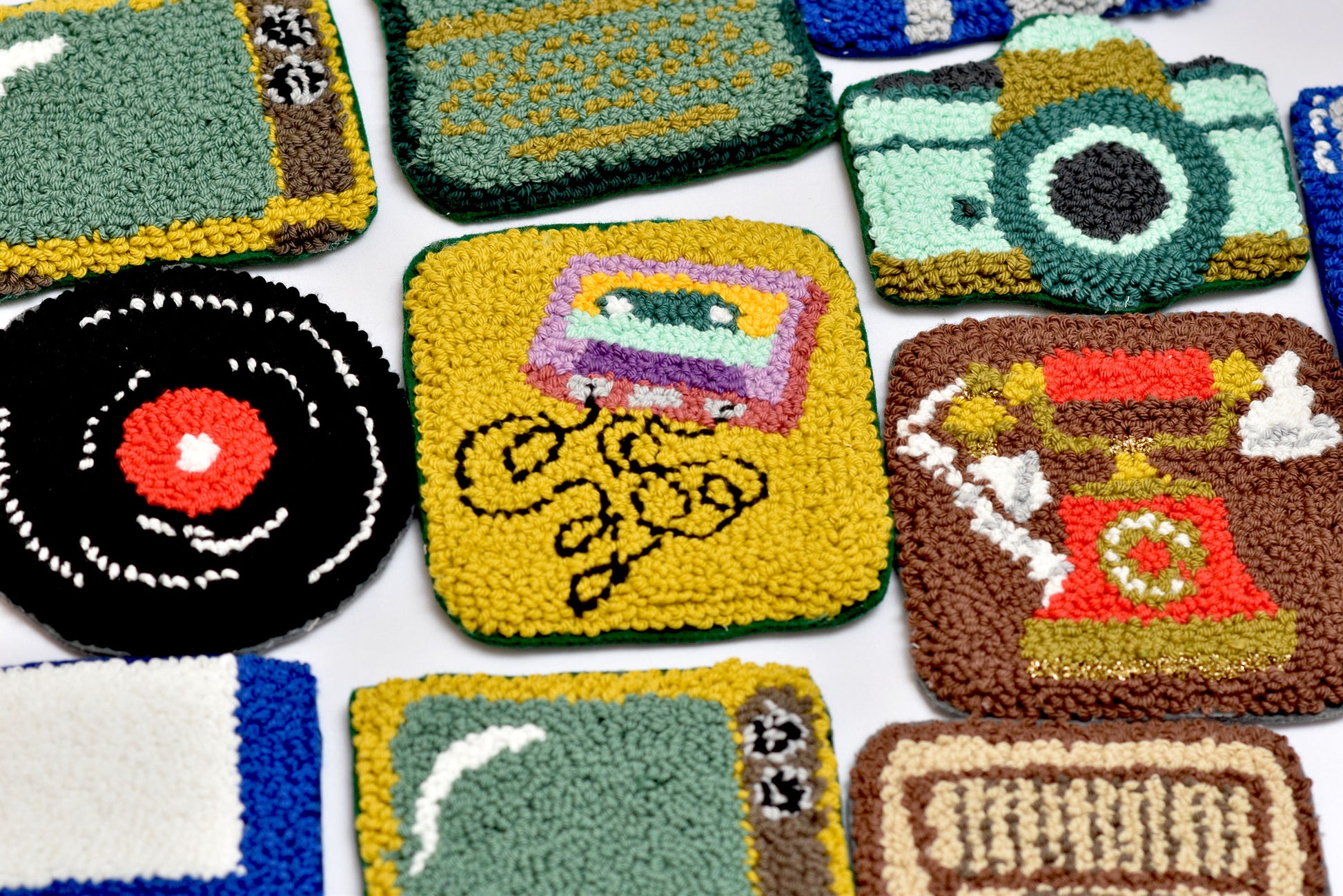 Collection of colorful, punch needled coasters with various designs and vintage devices themed on a white background