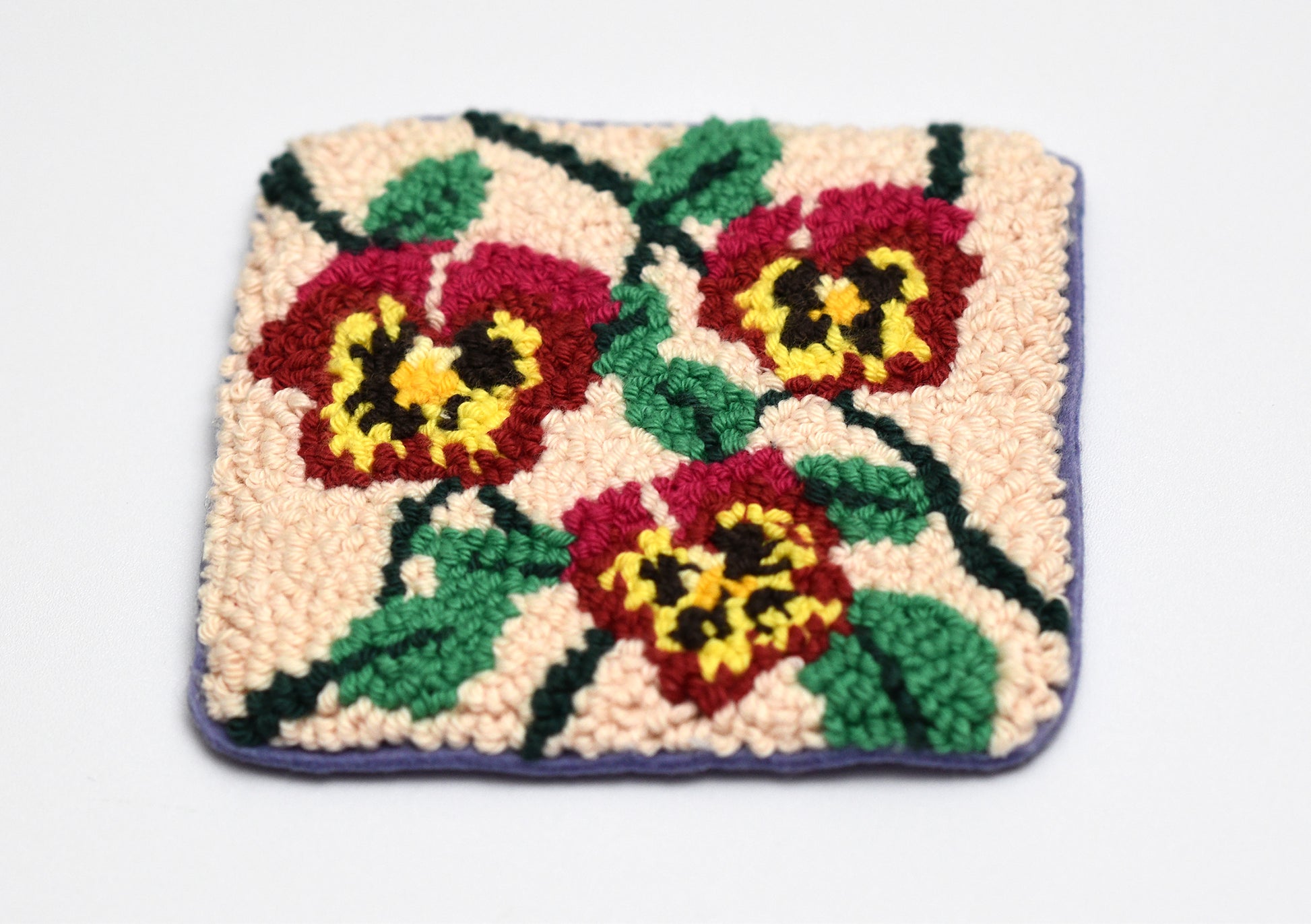 Square coaster with colorful viola flowers on a beige background