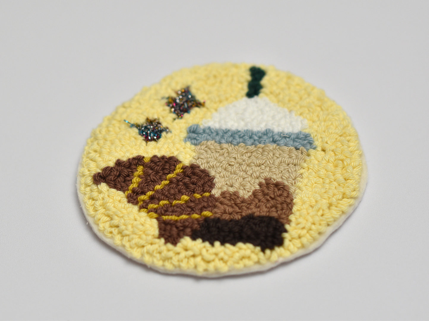 Round punch needle embroidery coaster with a coffee mug and croissant design on a yellow background