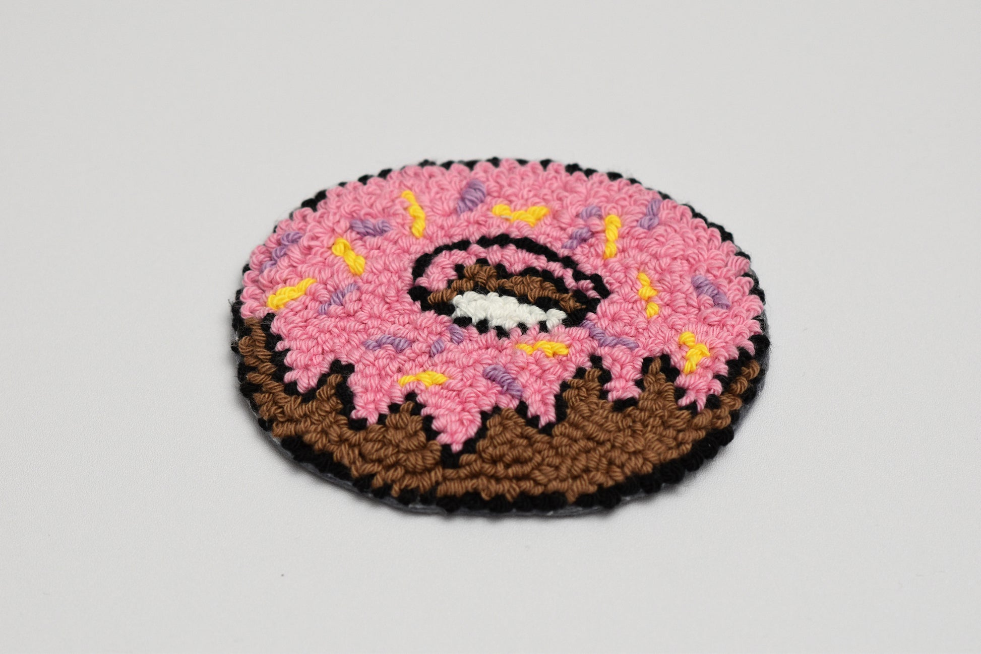Donut-shaped rug with pink icing and chocolate base on a light gray background