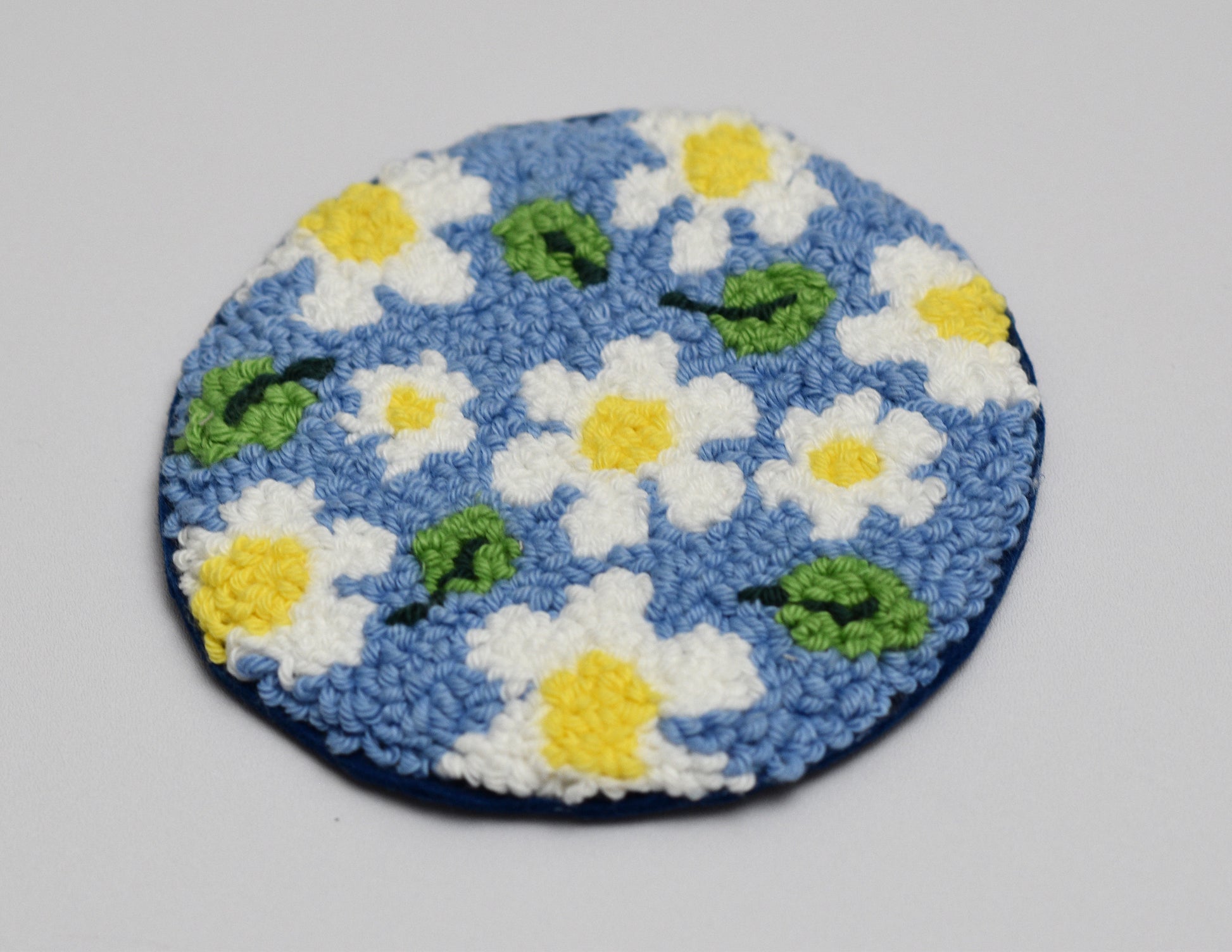 Round blue rug with white daisy flowers and green leaves on a light gray background