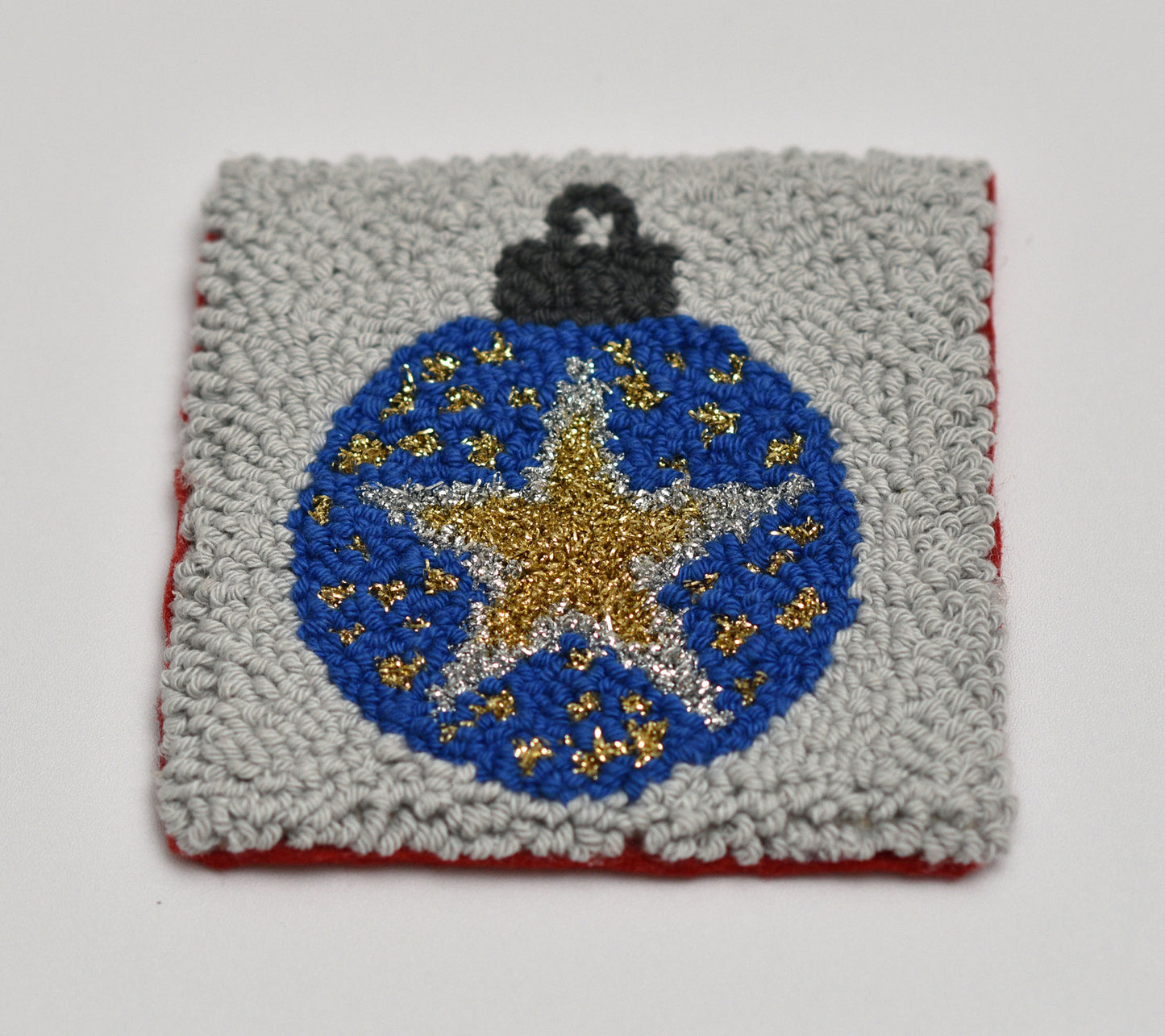 Punch needled square coaster with a blue ornament design featuring a gold star on a gray background