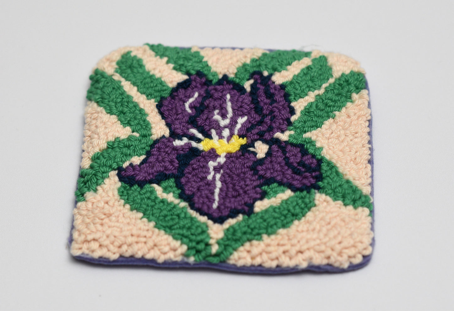 Square woven coaster with a purple iris flower design on a beige background