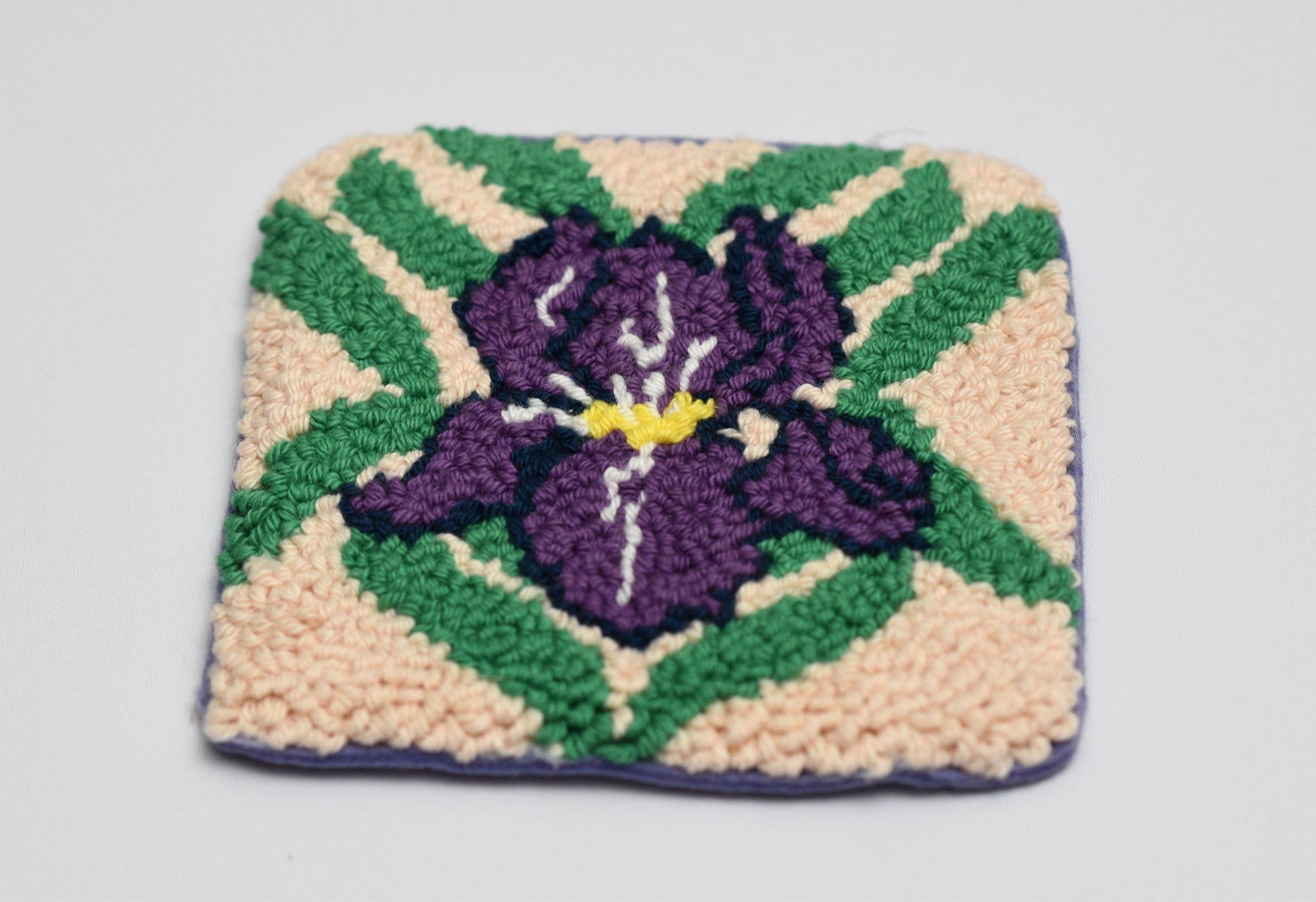 Square woven coaster with a purple iris flower design on a beige background