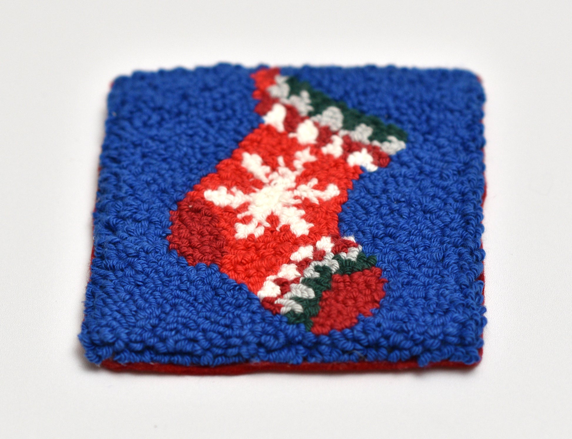 punch needle coaster with red and white Christmas stocking design on a blue background