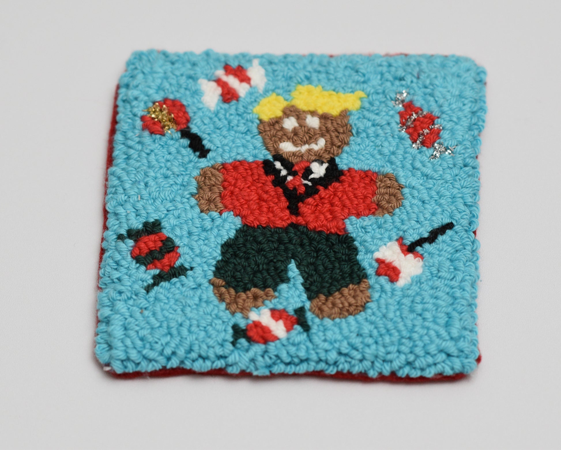 punch needle square coaster with a gingerbread man and lollipops on a light blue background
