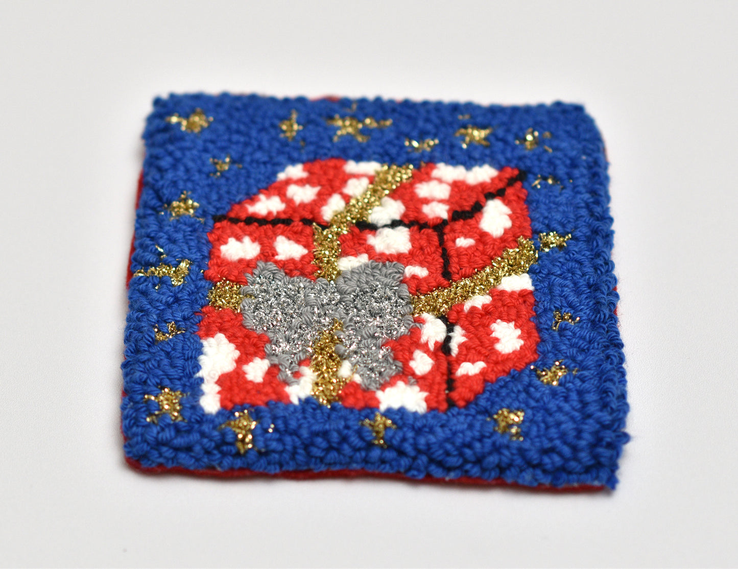 Punch needle coaster with red and white coloured gift package pattern on a blue background