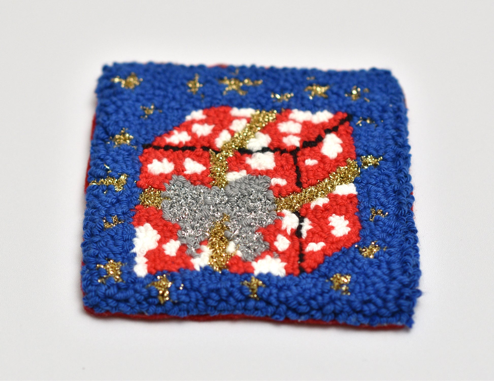 Punch needle coaster with red and white coloured gift package pattern on a blue background