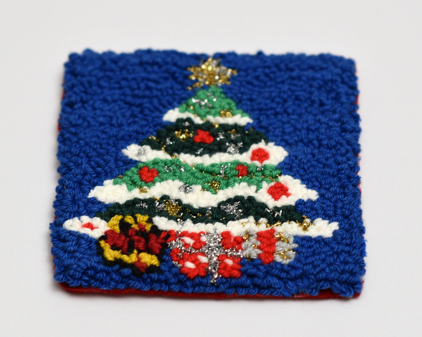 Embroidered punch needle coaster of a Christmas tree on a blue background