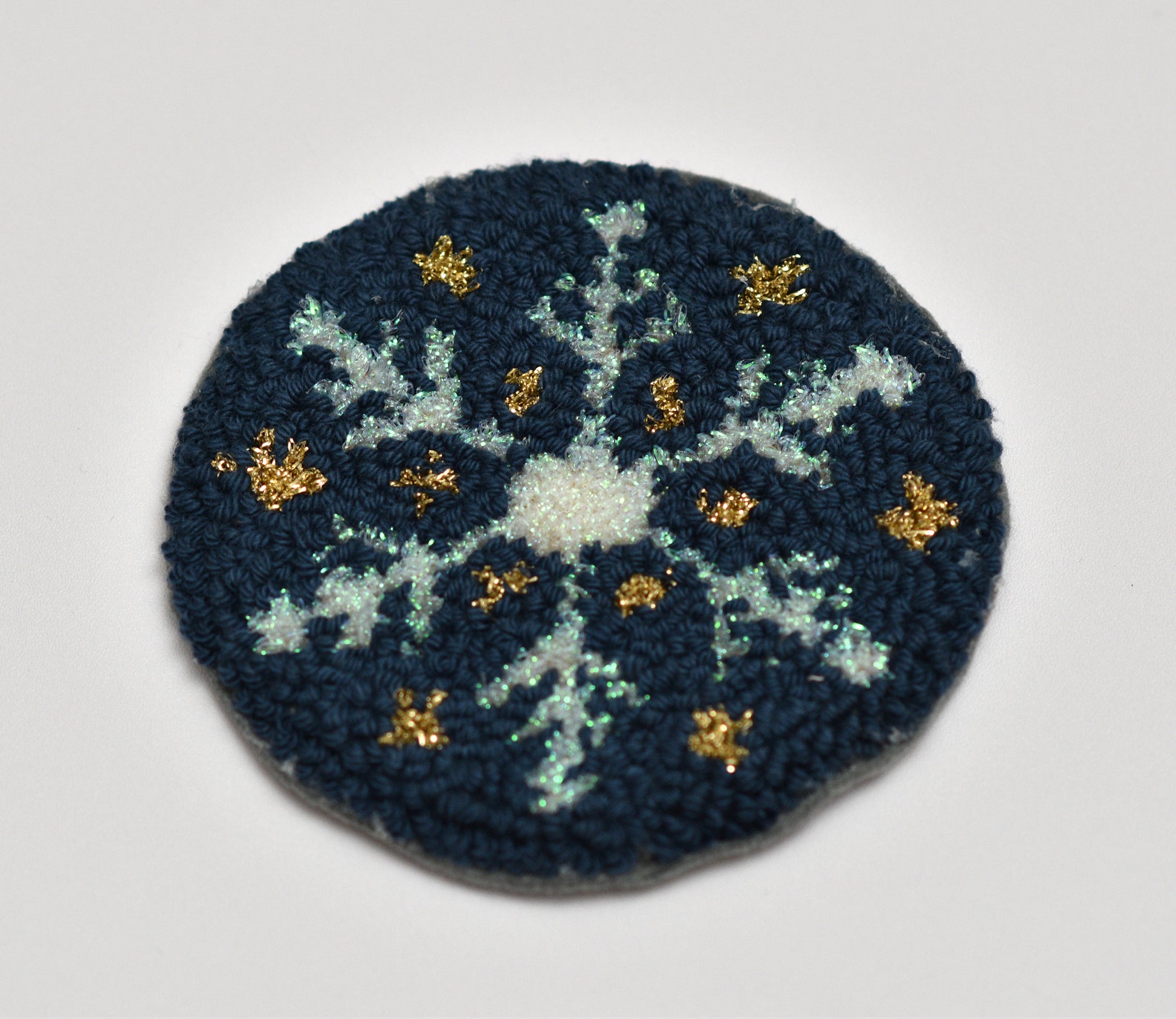 Circular embroidered punch needle coaster with snowflake design on a dark blue background