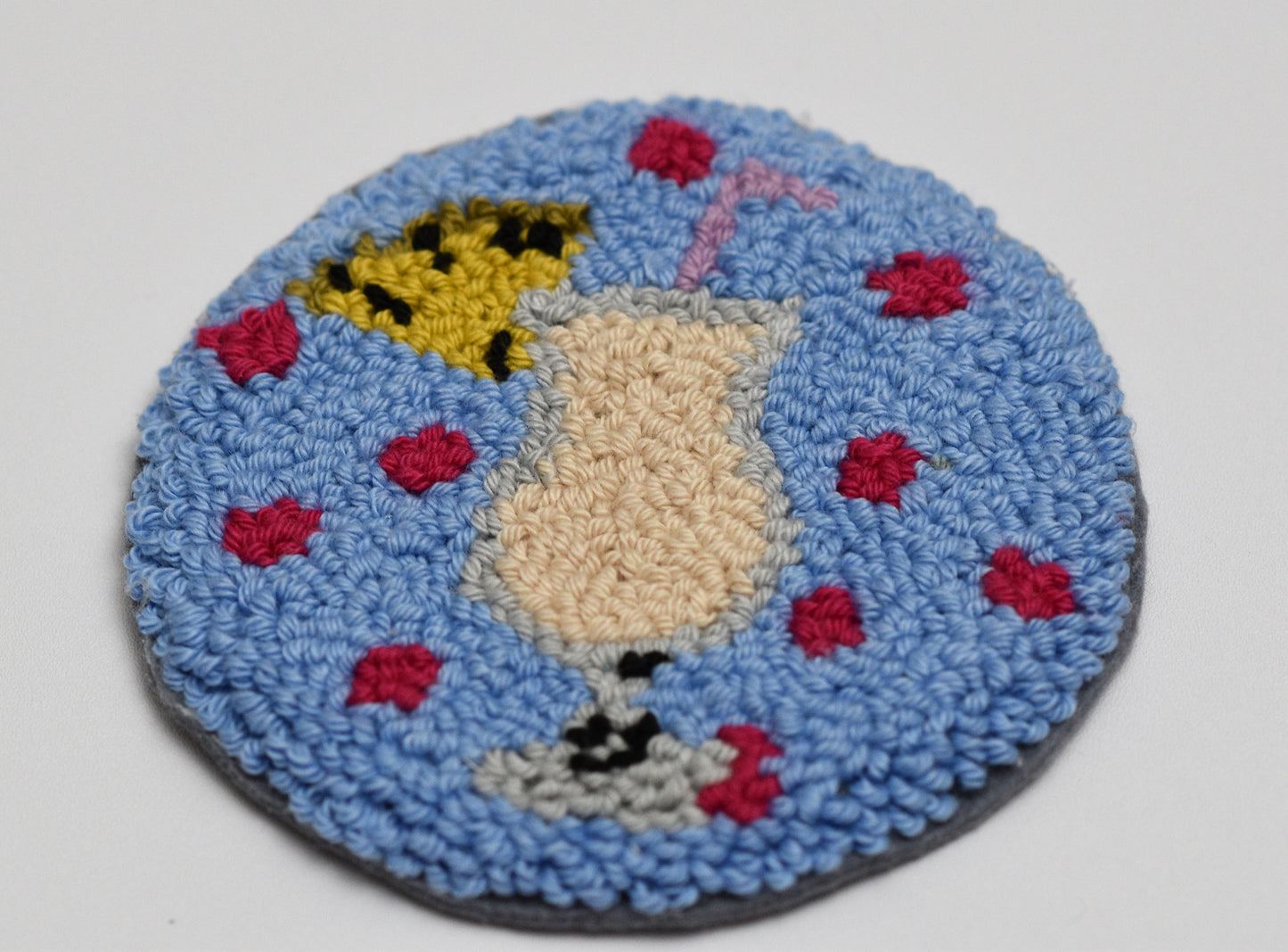 Round blue punch needled mug rug with a Piña Colada cocktail on a white background