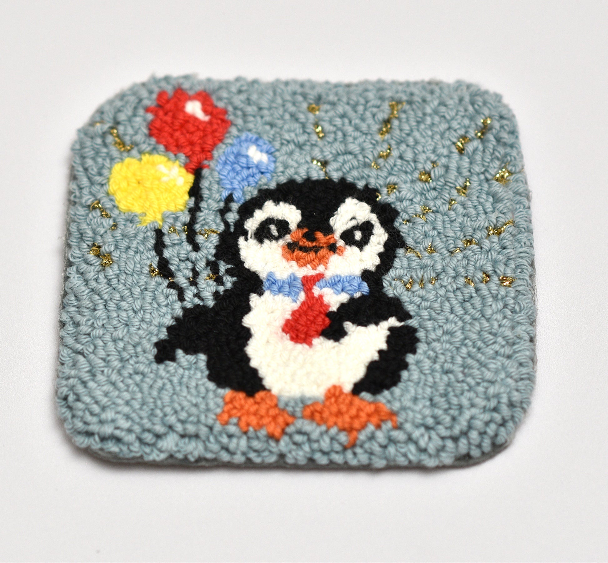 Embroidered coaster with a penguin holding balloons on a light blue background