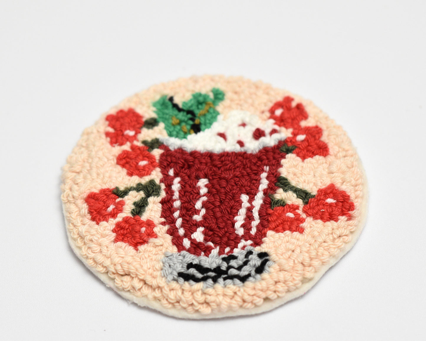 Round embroidered coaster with a cherry cocktail design on a beige background