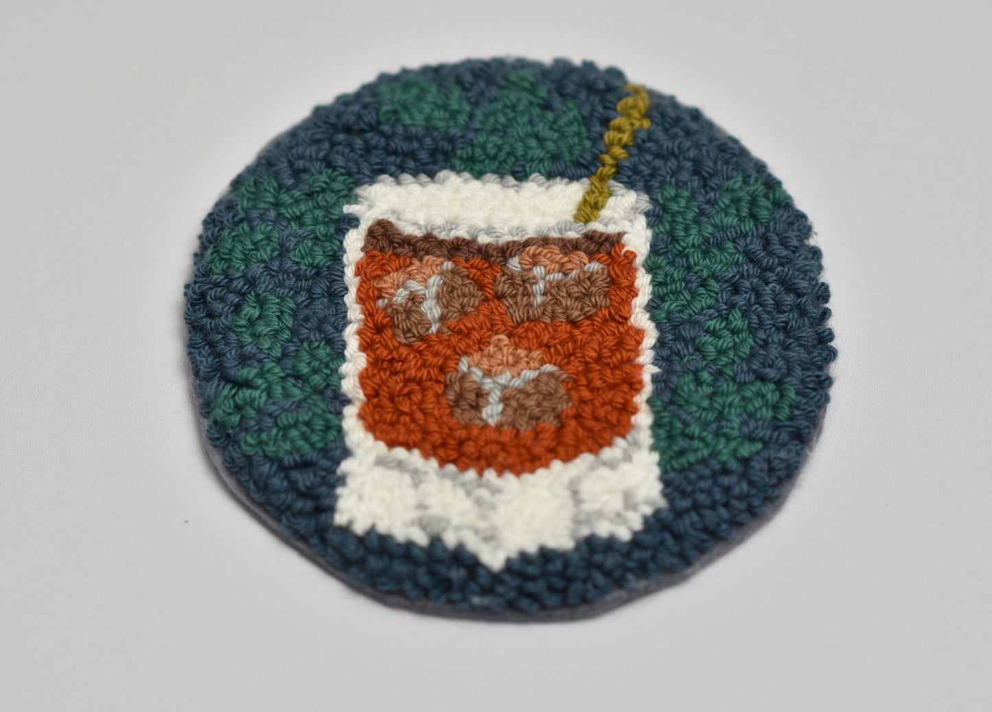 Punch needled round coaster with a design of a Whiskey on a white background